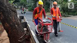 Pekerja mendorong mesin pengebor aspal untuk mengebor aspal yang menutup sumur resapan di Jalan Lebak Bulus III, Cilandak, Jakarta Selatan, Senin (6/12/2021). Sebanyak 29 sumur resapan yang tertutup aspal kembali dilubangi agar bisa bisa menampung air saat hujan. (merdeka.com/Arie Basuki)