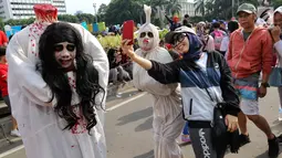 Warga berswafoto dengan seniman berkostum pocong saat kegiatan Car Free Day di Bundaran HI di Jakarta, Minggu, (12/11). Untuk dapat berswafoto warga dikenakan tarif semampunya. (Liputan6.com/Fery Pradolo)