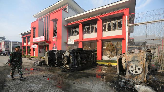 Prajurit TNI melintasi bangkai mobil yang rusak dampak kerusuhan di Lapas Narkotika Kelas III Langkat, Sumatera Utara, Kamis (16/5/2019). Akibat peristiwa kerusuhan yang dilakukan para narapidana di Lapas itu mengakibatkan tiga mobil petugas rusak terbakar dan ratusan napi melarikan diri. (AP Photo)