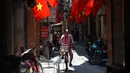 Seorang wanita mengendarai sepedanya melewati deretan bendera nasional Vietnam yang digantung di depan rumah untuk Hari Nasional Vietnam di pusat kota Hanoi (1/9/2020). Peringatan 75 tahun Hari Nasional Vietnam jatuh pada tanggal 2 September 2020. (AFP Photo/Nhac Nguyen)