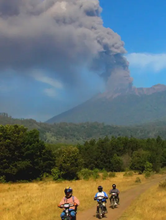 Sejumlah pengendara motor melintas dengan latar belakang Gunung Raung yang mengeluarkan awan panas yang terlihat dari Kabupaten Bondowoso, Jawa Timur, Minggu (12/7/2015). (AFP PHOTO/WIDARSHA)