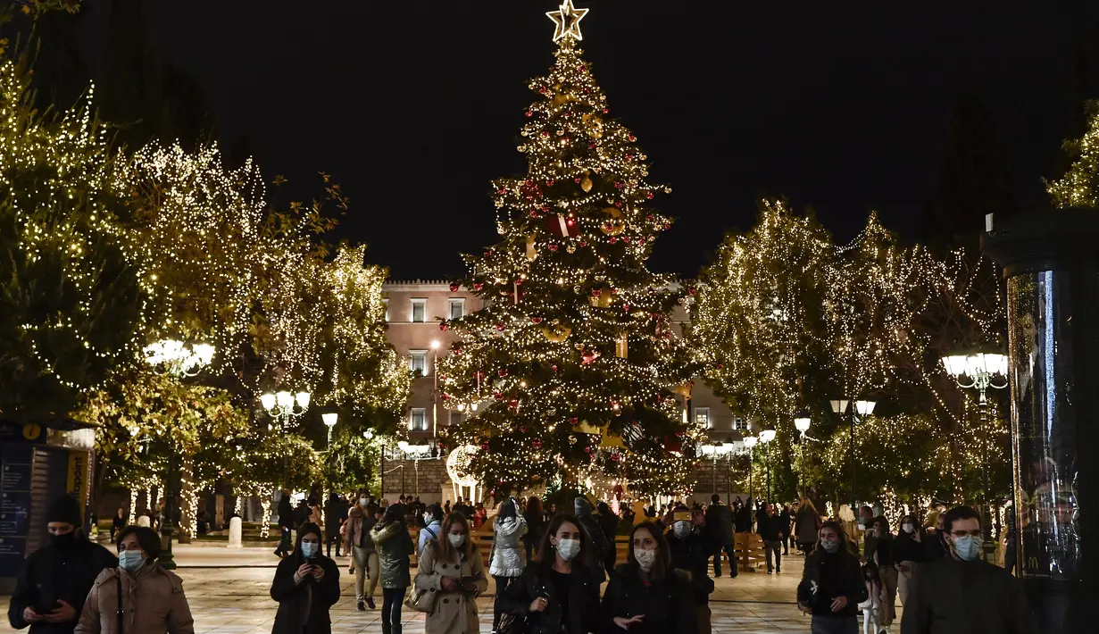 Orang-orang berjalan di alun-alun Syntagma yang diterangi dekorasi Natal di pusat kota Athena, Yunani pada 21 Desember 2020. Yunani akan merayakan musim Natal di bawah langkah-langkah penguncian wilayah atau lockdown COVID-19 hingga 7 Januari 2021 mendatang. (LOUISA GOULIAMAKI/AFP)