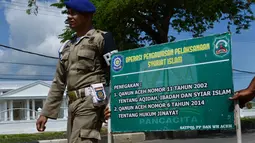 Polisi syariah membawa papan sosialisasi saat melakukan razia busana muslim di sepanjang jalan Lambaro, provinsi Aceh, Selasa (23/7/2019). Aceh merupakan satu-satunya provinsi di Indonesia yang memberlakukan hukum Syariat Islam bagi warganya. (Photo by CHAIDEER MAHYUDDIN / AFP)