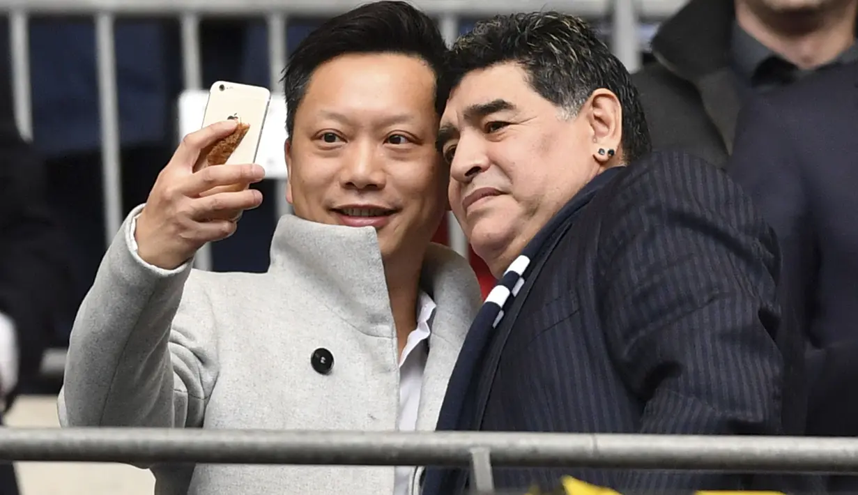 Legenda sepak bola Diego Maradona (kanan) berfoto selfie dengan fans saat menonton laga Premier League antara Tottenham melawan Liverpool di Wembley Stadium, London, (22/10/2017). (AFP/Ben Stansall)