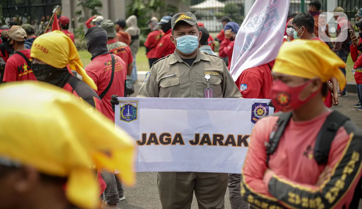 Petugas Satpol PP memegang poster imbauan protokol kesehatan COVID-19 saat unjuk rasa buruh di depan Gedung DPR, Jakarta, Selasa (17/11/2020). Pemerintah terus mengingatkan pentingnya 3M yaitu memakai masker, menjaga jarak, dan mencuci sebagai upaya pencegahan Covid-19. (Liputan6.com/Faizal Fanani)