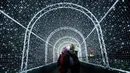 Pengunjung berjalan melewati terowongan yang dipenuhi cahaya lampu di Kew Gardens, London (21/11). Jelang perayaan Natal, Kew Gardens atau The Royal Botanical Garden dihiasi seni intalasi cahaya. (AP Photo/Frank Augstein)