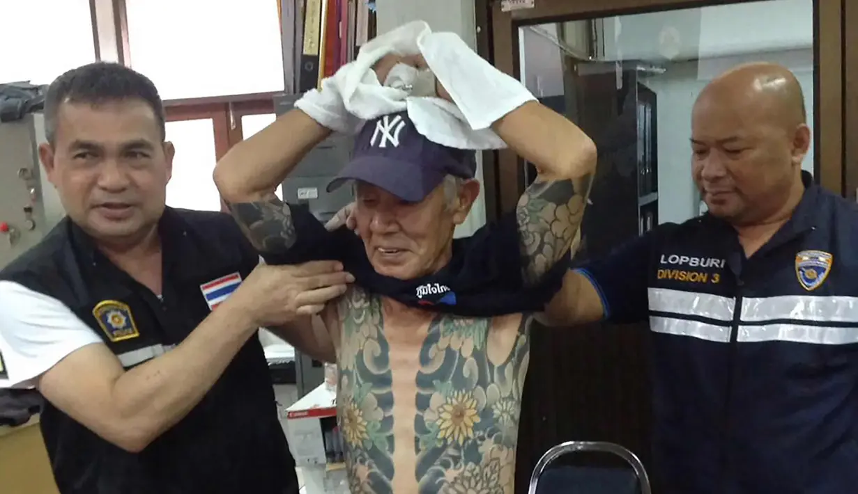 Petugas membuka baju Shigeharu Shirai yang dipenuhi tato di sebuah kantor polisi saat konferensi pers di Lopburi, Thailand, Kamis, (11/1). Shigeharu Shirai  tertangkap gara-gara foto tato di sekujur tubuhnya menjadi viral di media sosial. (AFP Photo)