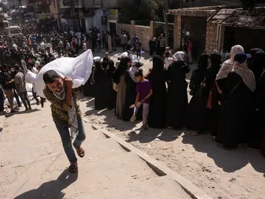 Seorang pria Palestina membawa sekantong tepung, sementara yang lain menunggu di depan titik distribusi yang didirikan oleh Save Youth Future Society (SYFS), yang bekerja sama dengan Program Pangan Dunia PBB (WFP), di Kota Gaza pada 26 Juni 2025. (BASHAR TALEB/AFP)