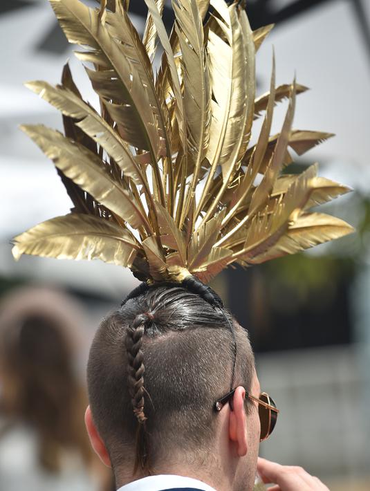 Seorang pria memakai hiasan kepala bulu berwarna emas saat menyaksikan balap kuda Melbourne di arena pacuan kuda Flemington Racecourse di Melbourne, Australia (1/11). (AFP/Paul Crock)