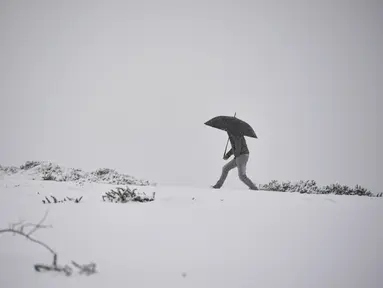 Seorang pria berlindung di bawah payung saat berjalan melalui lanskap bersalju dekat perbatasan Prancis di Ibaneta, Spanyol utara, Rabu (8/12/2021). Pihak berwenang telah mengumumkan salju dan hujan lebat selama beberapa hari ke depan di utara negara itu. (AP Photo/Alvaro Barrientos)