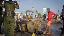 Tentara dan seorang anak berdiri dekat puing-puing kendaraan di lokasi ledakan bom mobil dekat pos pemeriksaan parlemen dan Kementerian Dalam Negeri di Ibu Kota Somalia, Mogadishu, Minggu (25/3). Serangan menewaskan empat orang. (AP/Farah Abdi Warsameh)