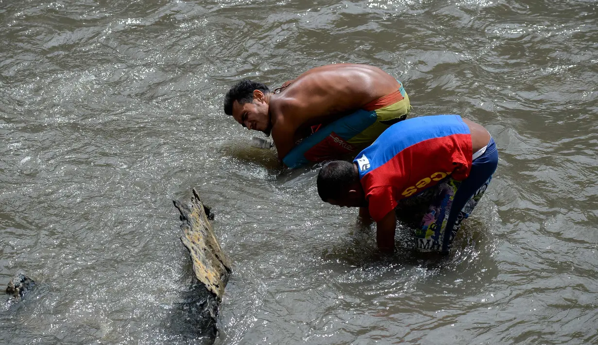 Dua pria mencari logam berharga di Sungai Guaire, di Caracas, Venezuela (1/2). Puluhan warga mencari logam atau tembaga setiap hari di Sungai Guaire, tempat selokan Caracas mengalir.  (AFP Photo/Federico Parra)