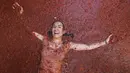 Seorang peserta berbaring di genangan tomat yang tergencet selama "Tomatina" tahunan, pesta pertarungan tomat di desa Bunol dekat Valencia, Spanyol, Rabu (31/8/2022). La Tomatina adalah festival lempar tomat Spanyol yang berlangsung setiap tahun pada hari Rabu terakhir bulan Agustus. (AP Photo/Alberto Saiz)