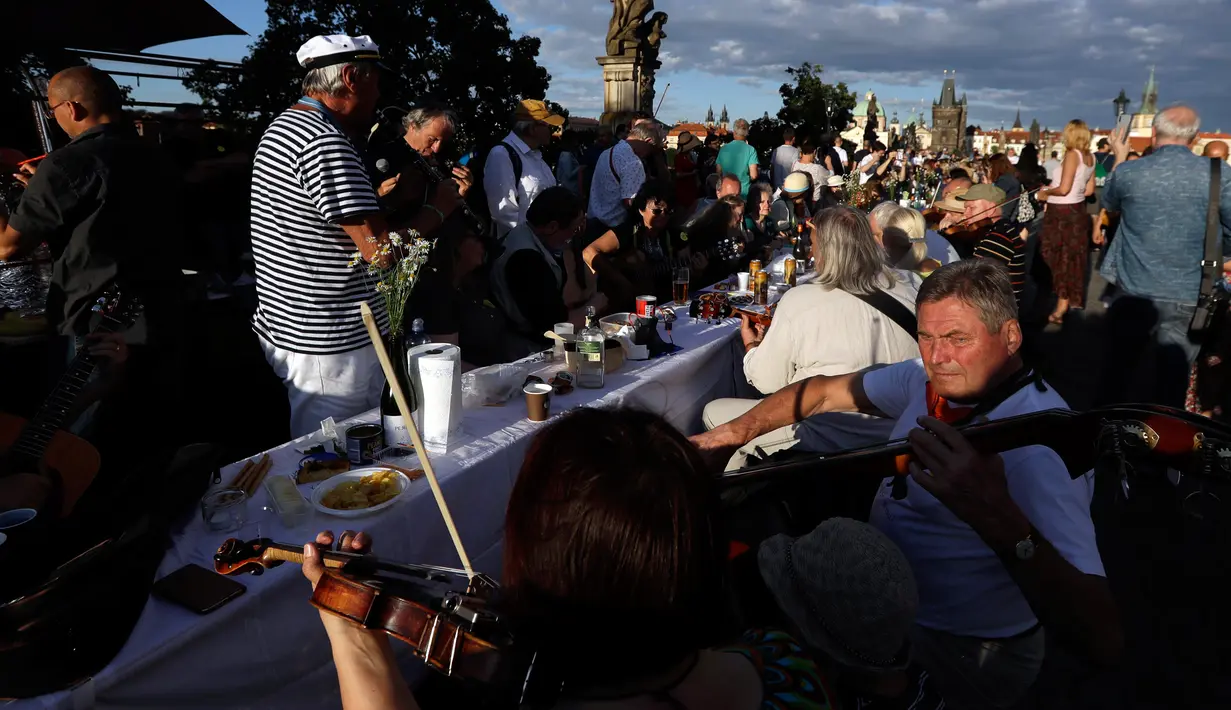 Warga memainkan musik saat makan malam bersama di atas meja sepanjang 500 meter di Charles Bridge di Praha, Republik Ceko, Selasa (30/6/2020). Kegiatan itu merupakan perpisahan simbolis yang digelar untuk menandai akhir dari masa krisis virus corona Covid-19 di negara tersebut. (AP/Petr David Josek)