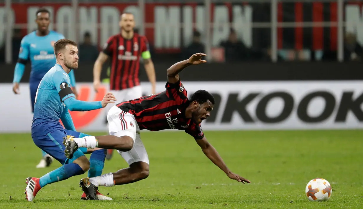 Pemain AC Milan, Franck Kessie tersungkur saat berebut bola dengan pemain Arsenal Aaron Ramsey pada pertandingan Liga Europa leg pertama di stadion San Siro Milan, Italia (8/3). AC Milan takluk 0-2 dari Arsenal. ( AP Photo / Luca Bruno)