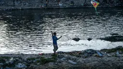 Seorang anak menerbangkan layang-layang di tepi sungai menjelang festival Hindu Dashain di Kathmandu (7/10/2020). Festival ini jatuh pada bulan September atau Oktober, dimulai dari shukla paksha (dua minggu bulan cerah) di bulan Ashwin dan berakhir pada Purnima, bulan purnama. (AFP/Prakash Mathema)