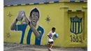 Seorang anak melewati mural bergambar Angel Di Maria menggunakan kostum Central Rosario di Santa Fe, Argentina, Minggu (5/4/2015). Central Rosario merupakan klub pertama Di Maria saat memulai karier profesional. (AFP Photo/Hector Rio)