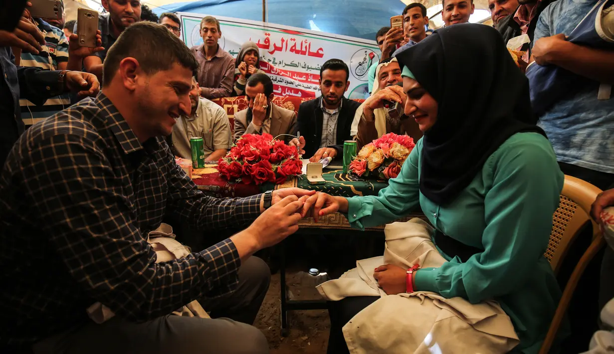 Petugas medis Muadh Al-Raqab memakaikan cincin kepada Hadeel Al-Najjar saat melangsungkan prosesi pernikahan di dalam tenda jalur Gaza selatan, Palestina (2/5). (AFP Photo/Said Khatib)