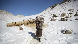 Seorang wanita menggendong putranya setelah memberi makan domba keluarganya di desa Amazigh Timahdite, Maroko (4/12/2021). Bagi masyarakat desa Timahdite Maroko ketika hujan salju lebat mereka bisa berminggu-minggu atau berbulan-bulan untuk isolasi. (AP Photo/Mosa'ab Elshamy)