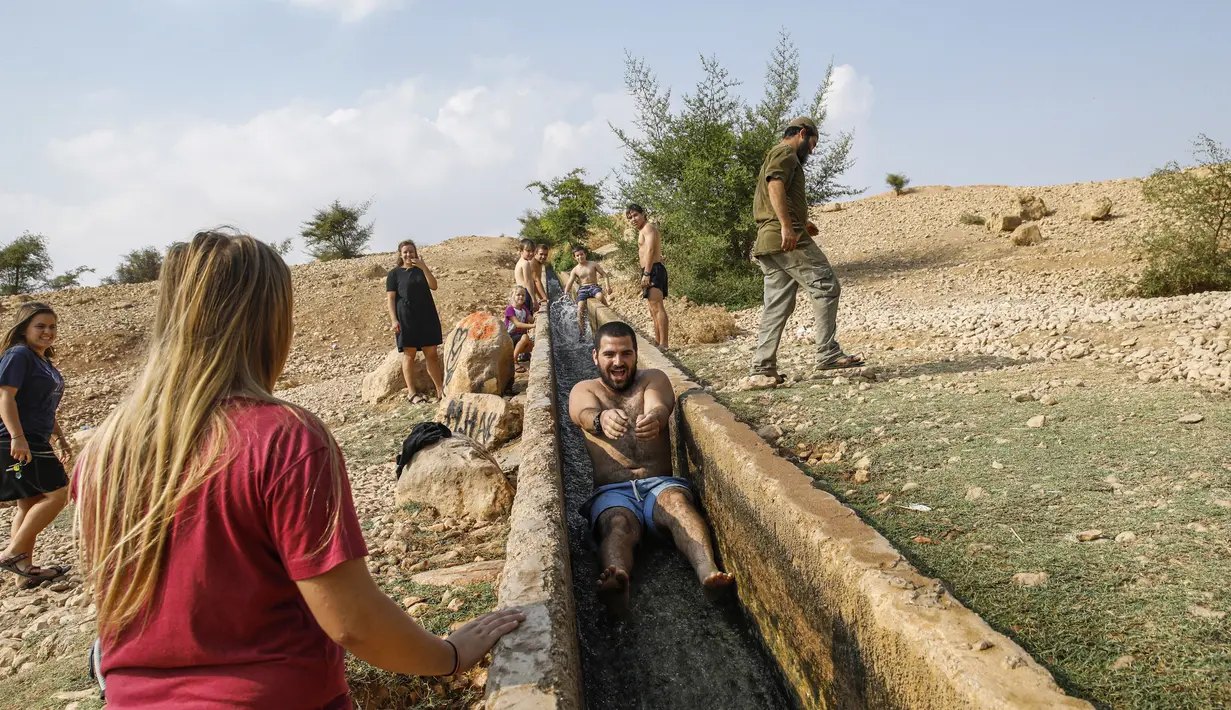 Seorang pria meluncur saat menikmati bermain air di sebuah kanal kecil di Desa Al-Auja selama perayaan keagamaan Yahudi dalam Festival Sukkot di Tepi Barat (17/10/2019). (AFP Photo/Menahem Kahana)