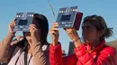 Dua orang wanita melihat gerhana matahari annular dengan alat khusus di Estancia El Muster, Argentina (26/2). Menggunakan teleskop khusus, kaca mata pelindung, atau perangkat buatan sendiri, mereka menyaksikan fenomena alam tersebut. (AFP/Alejandro Pagni)