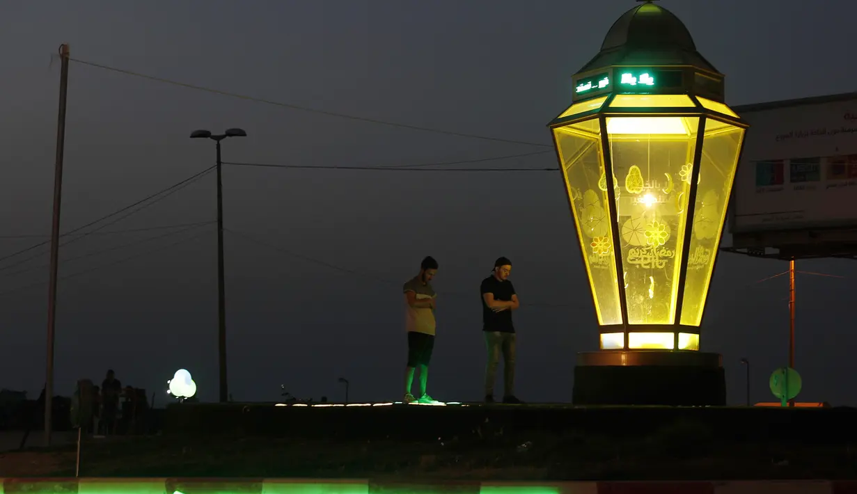 Sejumlah anak muda melaksanakan salat dekat lentera Ramadan tradisional di pantai Kota Gaza, Palestina, Kamis (21/5/2020). Di tengah pandemi COVID-19, berbuka puasa bersama di pantai Kota Gaza tetap ramai. (AP Photo/Adel Hana)