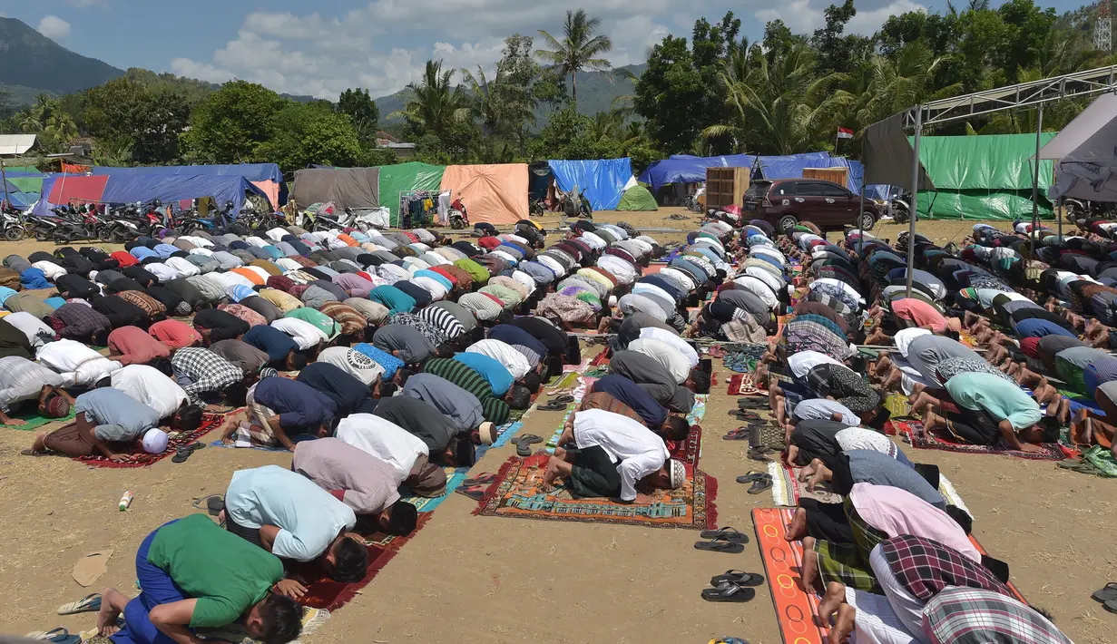 Umat muslim salat Jumat di sebuah ladang di dekat tempat penampungan sementara setelah gempa di Pemenang, Lombok (10/8). Menurut menteri senior, korban tewas akibat gempa dahsyat 6,9 SR di pulau Lombok melonjak di atas 300 orang. (AFP Photo/Adek Berry)