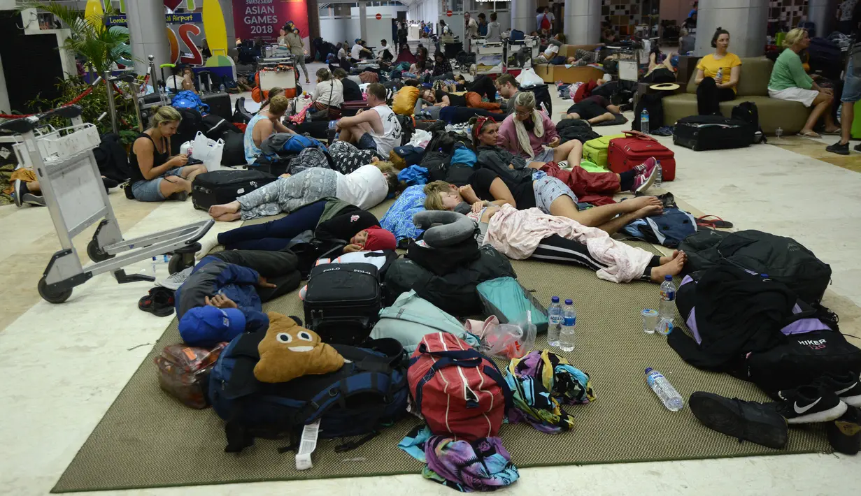 Turis asing bersantai dengan alas seadanya di lantai Bandara Internasional Lombok Praya, NTB, Senin (6/8). Imbas gempa 7 skala Richter, para wisatawan mancanegara terlantar di bandara karena jam pemberangkatan pesawat yang tertunda. (AFP/SONNY TUMBELAKA)