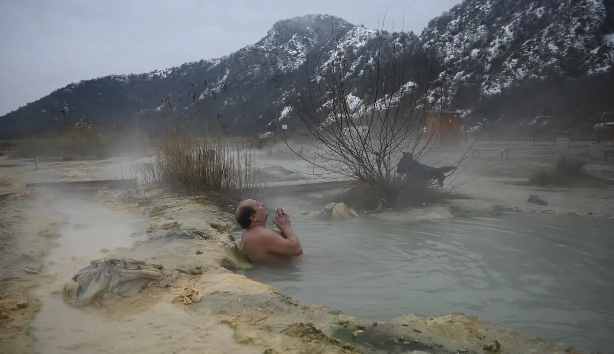 Seorang pria menikmati air panas di mata air mineral alami pada hari musim dingin di dekat desa Rupite, Bulgaria (2/2/2022). Penduduk setempat percaya bahwa air mineral menyembuhkan banyak penyakit dan gangguan. (AFP/Nikolay Doychinov)