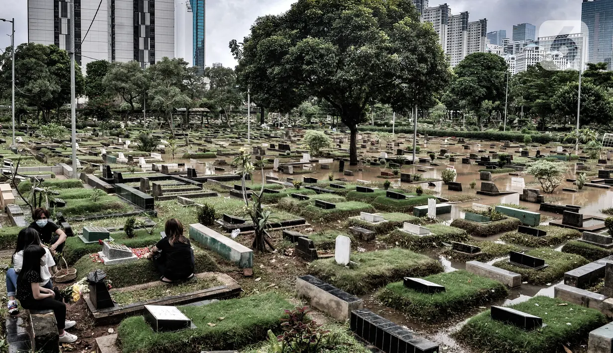 Warga berziarah di makam keluarga di dekat lokasi banjir yang merendam TPU Karet Bivak, Jakarta, Minggu (7/2/2021). Banjir yang terjadi di TPU Karet Bivak untuk kedua kalinya tersebut juga menyulitkan mereka yang ingin melakukan ziarah ke makam keluarga maupun kerabat. (merdeka.com/Iqbal Nugroho)