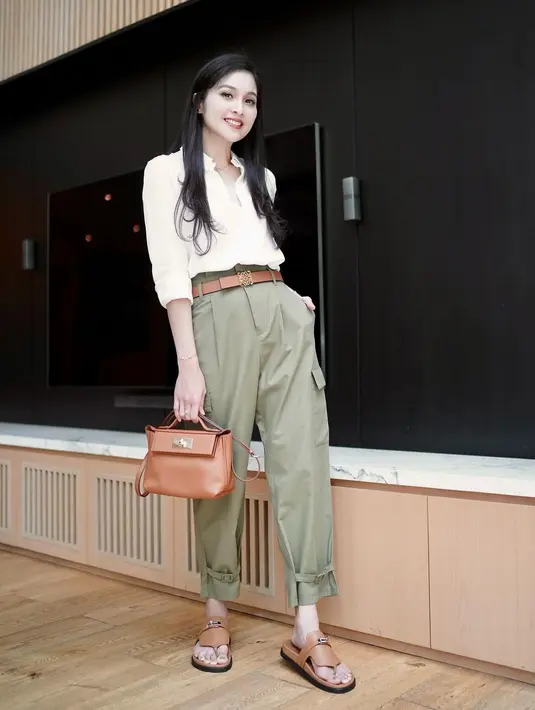 Sandra Dewi menawan dalam balutan kemeja putih lengan panjang yang dilipat. Ia padukan penampilannya dengan celana berwarna hijau sage, handbag, belt, dan sandal cokelat yang serasi. [Foto: Instagram/sandradewi88]