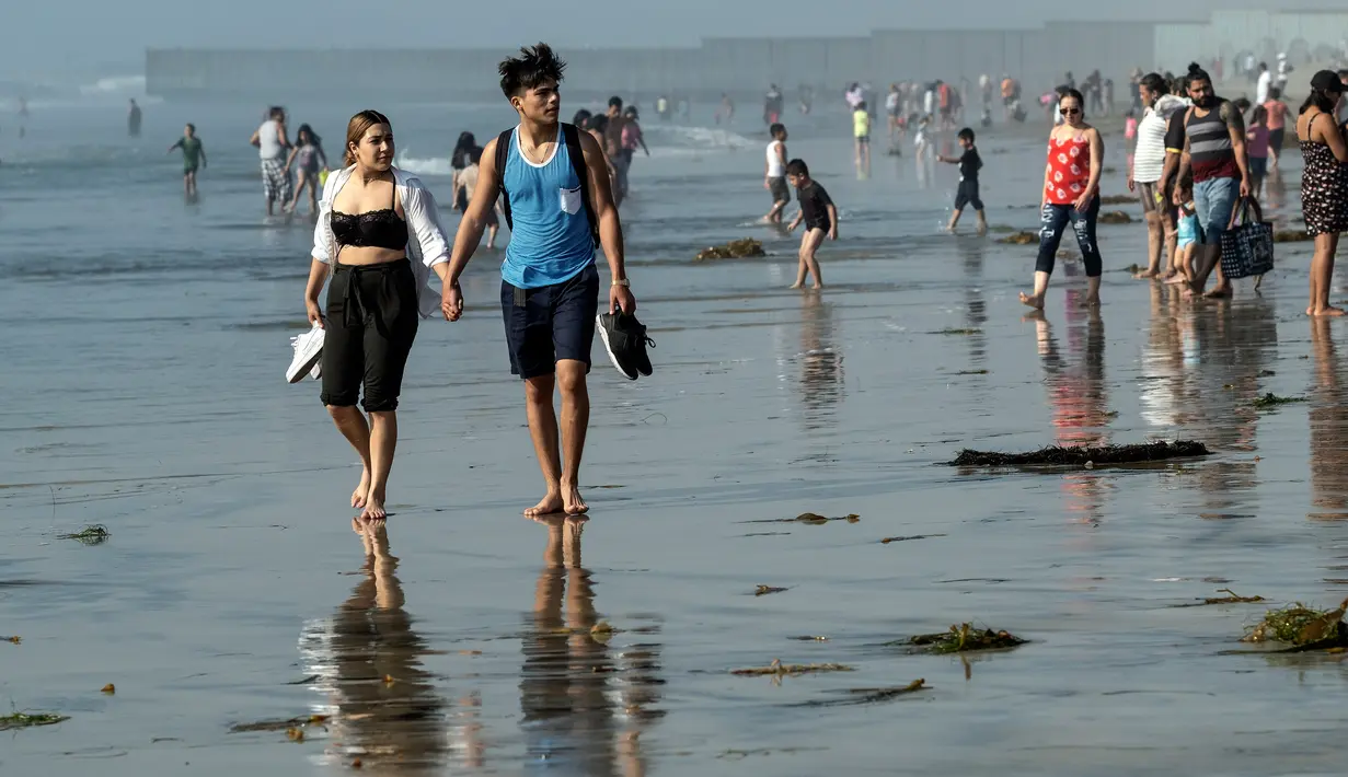 Orang-orang mengunjungi pantai di Playas de Tijuana dekat perbatasan AS-Meksiko di Tijuana Meksiko, Sabtu (3/10/2020). Akhir pekan ini pantai di Playas de Tijuana dibuka kembali dengan pembatasan pengunjung, setelah ditutup sejak Maret lalu guna mencegah penyebaran Covid-19. (Guillermo Arias/AFP)