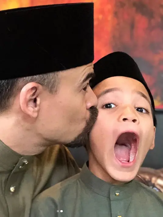 Suami Bunga Citra Lestari, Ashraf Sinclair mencium putranya Noah Aidan Sinclair saat berpose dengan mengenakan busana serasi dan peci hitam. (Instagram/@ashrafsinclair)