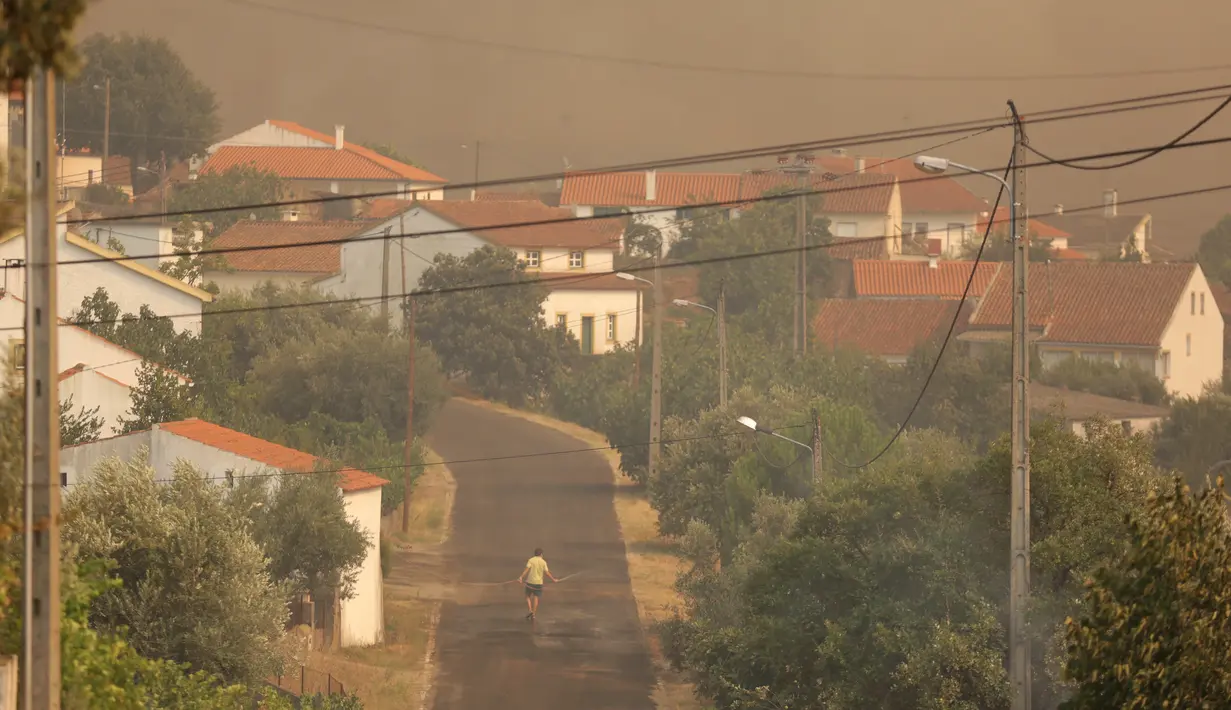 Warga menggunakan membasahi daerah di sekitar rumahnya saat kebakaran melanda di sekitar desa Sao Jose das Matas, dekat Macao, Portugal tengah, (26/7). Lebih dari 2.300 petugas pemadam kebakaran menangani kebakaran tersebut. (AP Photo/Armando Franca)