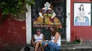 Dua wanita duduk di samping mural karya 'Meninas' selama festival seni jalanan tahunan Meninas de Canido di Ferrol, Spanyol, Minggu (2/9). (MIGUEL RIOPA/AFP)