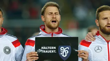 Bek Jerman,  Benedikt Hoewedes memegang tulisan ucapan turut berbelasungkawa kepada para korban jatuhnya pesawat Germanwings di Pegunungan Alpen di Stadion Fritz-Walter, Kamis (26/3/2015). Jerman bermain Imbang 2-2 atas Australia. (REUTERS/Ralph Orlowski)