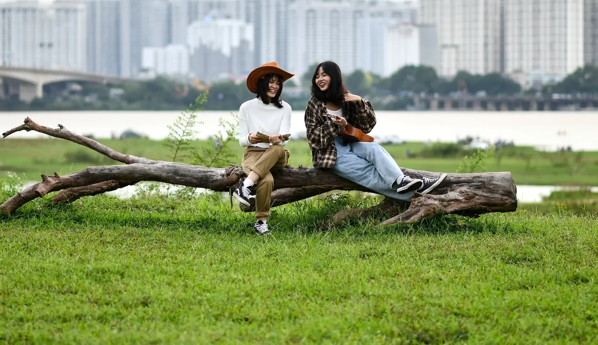 Para gadis berbagi momen ringan sambil berpose untuk berfoto di lapangan terbuka di sepanjang tepi sungai Merah di Hanoi (13/0/2020). (AFP/Manan Vatsyayana)