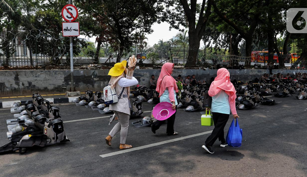 Warga melintasi polisi yang tengah bersiaga di sekitar Gedung DPR RI, Jakarta, Kamis (17/10/2019). Polisi kembali menutup sejumlah ruas jalan menuju kawasan Gedung DPR RI guna menjaga kondusifitas jelang pelantikan Presiden dan Wakil Presiden terpilih. (Liputan6.com/JohanTallo)