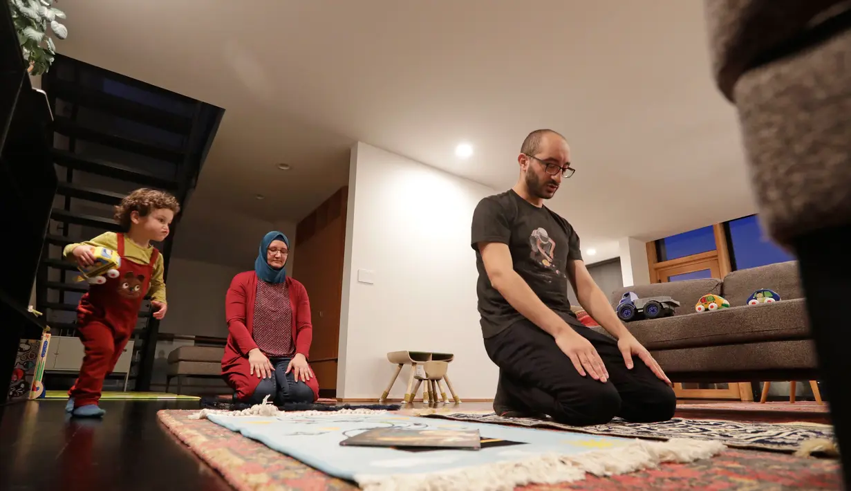 Ahmad Kamel (depan) melaksanakan salat Maghrib dengan istrinya, Nadia Chaouch, ketika putra mereka Ahmad Kamel berlari melewati setelah keluarga berbuka puasa saat bulan Ramadan selama wabah Covid-19 di rumah mereka di Seattle (28/4/2020). (AP/Elaine Thompson)