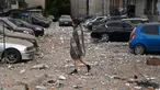 Seorang penduduk lokal berjalan di antara mobil-mobil yang rusak saat meninggalkan bangunan tempat tinggal bertingkat, yang sebagian hancur setelah serangan pesawat tak berawak pada malam hari di Kyiv pada 30 Mei 2023. (Sergei SUPINSKY/AFP)