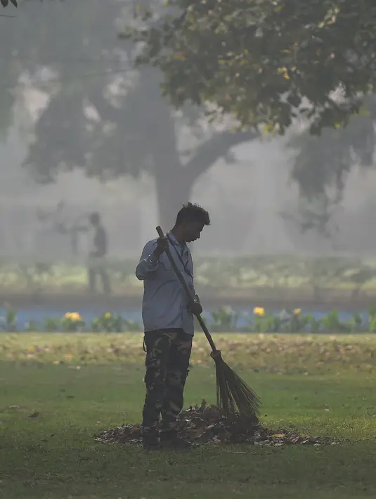 Seorang pekerja menyapu halaman dalam kondisi kabut asap tebal di New Delhi, Selasa (12/11/2019). Kabut asap kembali menyelimuti ibu kota India setelah akhir pekan dengan udara cerah dan cuaca yang lebih baik. (Photo by Money SHARMA / AFP)