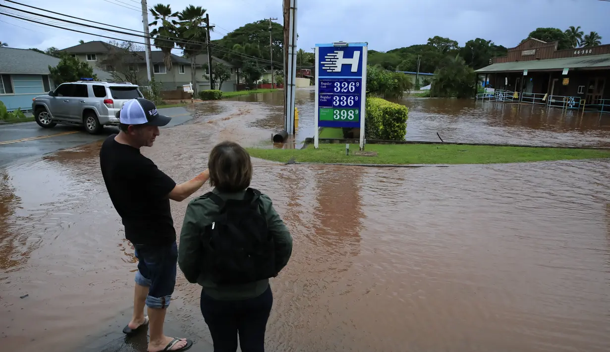 Orang-orang berdiri di tepi air banjir di sepanjang Jalan Haleiwa di Hawaii (9/3/2021). Hujan deras telah menggenangi beberapa bagian Hawaii selama beberapa hari terakhir. (Jamm Aquino/Honolulu Star-Advertiser via AP)