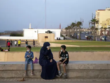 Sekeluarga memakai masker untuk mencegah penyebaran virus corona sambil menikmati malam mereka di tepi cornice, di Rabat, Maroko, Selasa (22/9/2020). (AP Photo / Mosa'ab Elshamy)