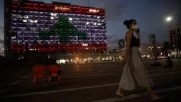 Seorang perempuan Israel berjalan saat Gedung Balai diterangi dengan bendera Lebanon di Tel Aviv, Rabu (5/8/2020). Cahaya bendera Lebanon diproyeksikan sebagai bentuk solidaritas atas ledakan dahsyat di  Beirut yang menghebohkan dunia.  (AP Photo/Sebastian Scheiner)