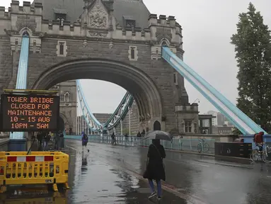 Orang-orang berjalan melewati papan tanda dekat Tower Bridge di Sungai Thames di London, Senin (9/8/2021). Tower Bridge London macet terbuka karena kesalahan teknis mengakibatkan gangguan lalu lintas di kedua sisi Sungai Thames karena mobil dan pejalan kaki tidak dapat menyeberang. (AP/Tony Hicks)