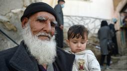 Seorang pria menggendong seorang anak saat petugas kesehatan (kanan atas) memberikan vaksin polio selama kampanye vaksinasi di kawasan tua Kabul, Afghanistan pada 8 November 2021. Vaksinasi tersebut merupakan yang pertama sejak Taliban berkuasa di Afghanistan. (WAKIL KOHSAR / AFP)