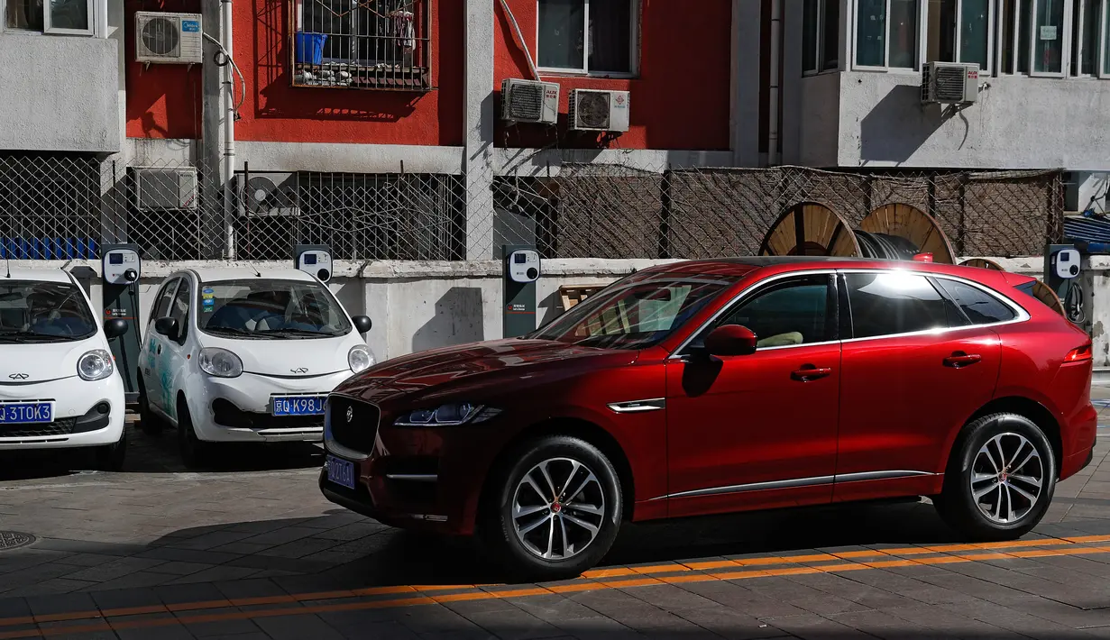 Sebuah mobil SUV warna merah melintas di depan mobil listrik model lama yang diparkir di stasiun pengisian listrik di rumah hunian Beijing (14/04/2017). Penjualan mobil kesulitan karena minimnya stasiun pengisian listrik. (AP Photo / Andy Wong)