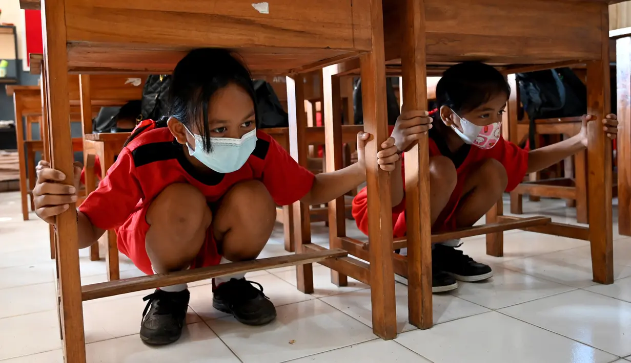 Anak-anak sekolah berlindung di bawah meja untuk melindungi diri mereka sat latihan gempa dan tsunami di Tanjung Benoa, Kabupaten Badung, Bali, 24 Mei 2022. (SONY TUMBELAKA/AFP)