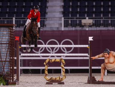 Atlet berkuda Kanada Mario Deslauriers mengendarai Bardolina 2 melewati patung pesumo dalam kualifikasi individu lompat berkuda Olimpiade Tokyo 2020 di Equestrian Park di Tokyo (3/8/2021). Pihak panitia memasang patung simbol Jepang seperti sakura sampai pesumo di arena lintasan. (AFP/Behrouz Mehri)
