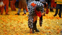 Seorang peserta mengumpulkan jeruk di tanah saat perang-perangan selama karnaval di kota Ivrea, Italia, Minggu (7/2). Peserta yang dibagi menjadi dua tim ini saling melempar jeruk menggunakan kostum dan aksesoris lengkap. (REUTERS/Stefano Rellandini)